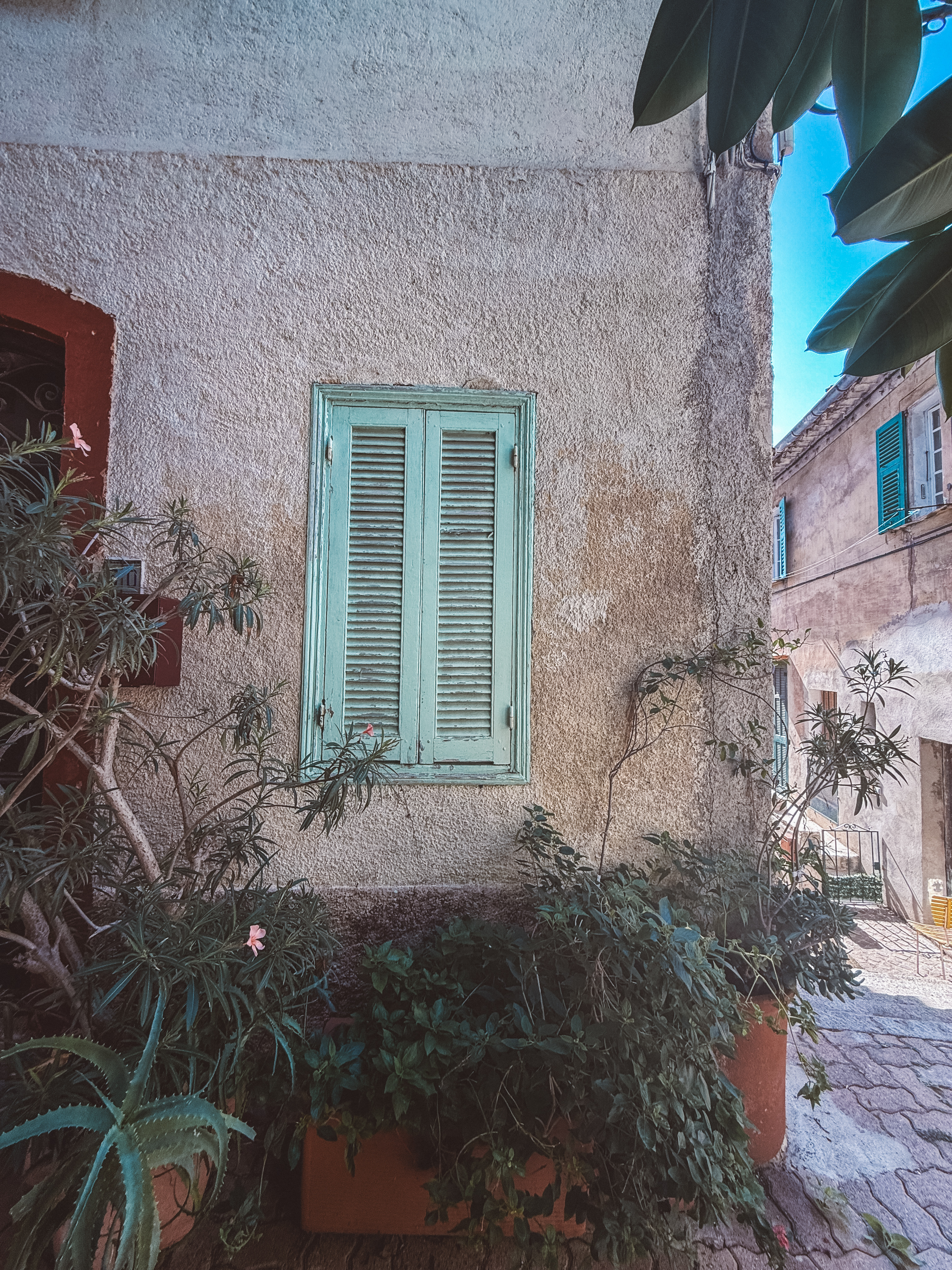 Pale green wooden shutters on a sun-washed stone facade in a French village