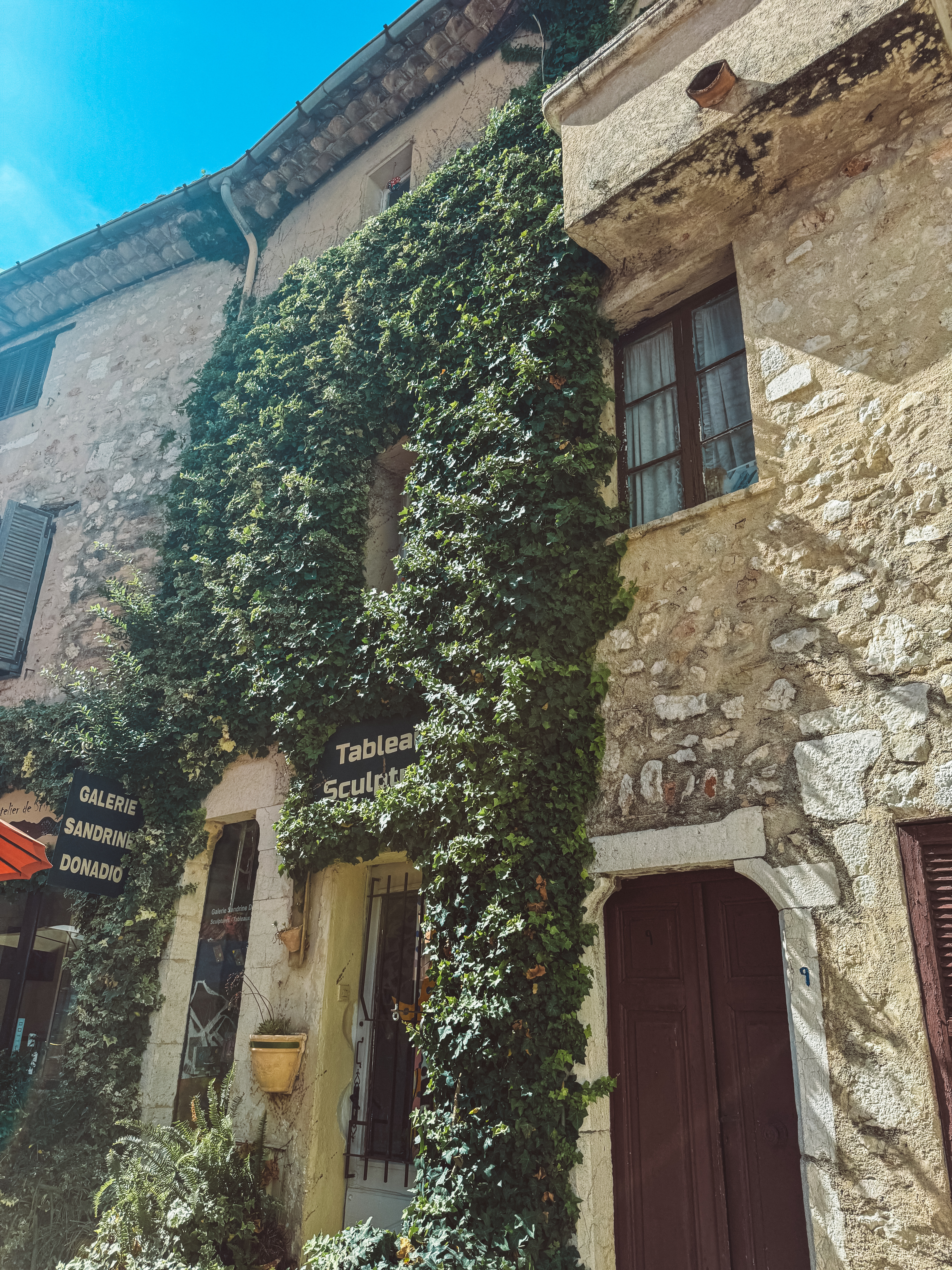 An ivy-covered stone building along a sunlit street in a South of France village