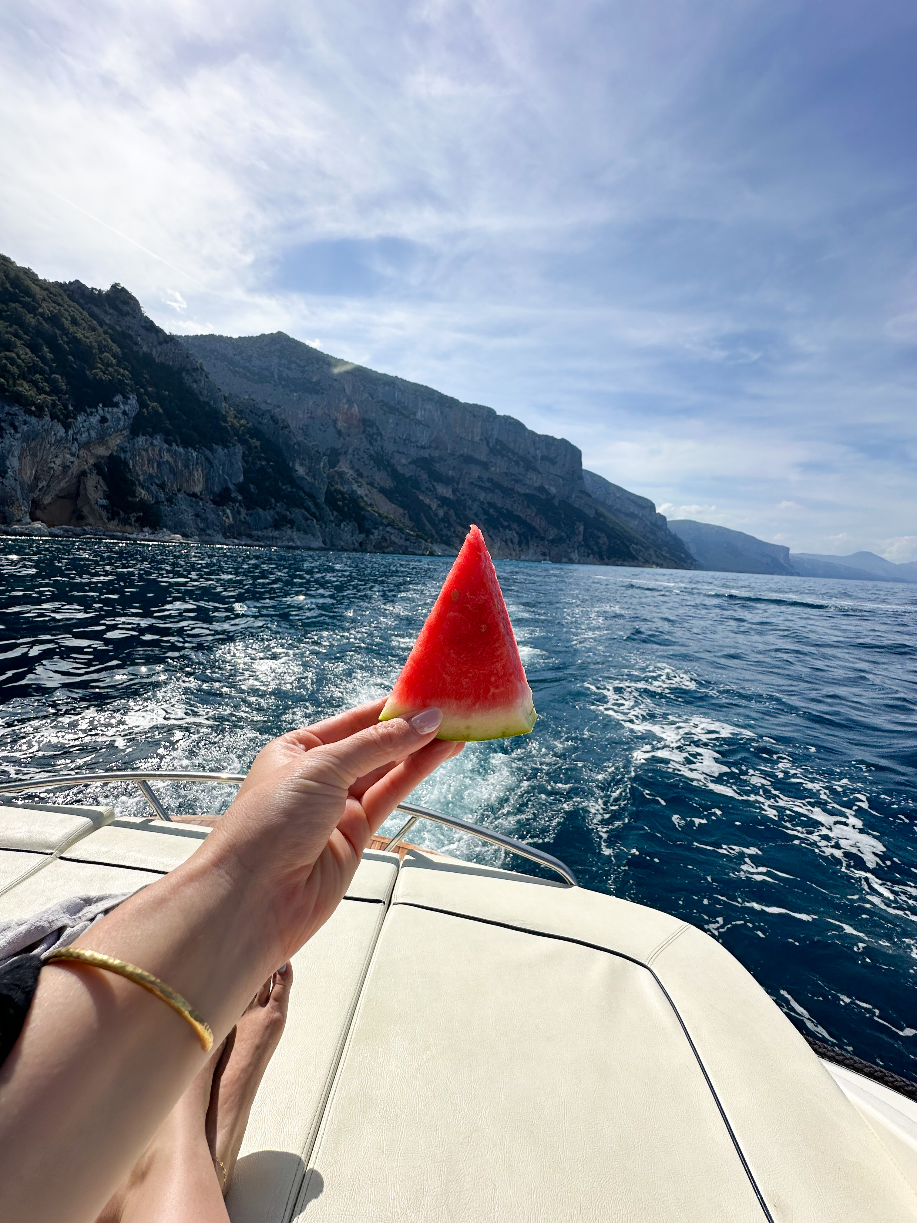 A slice of watermelon held up against the cliffside coastline from a boat