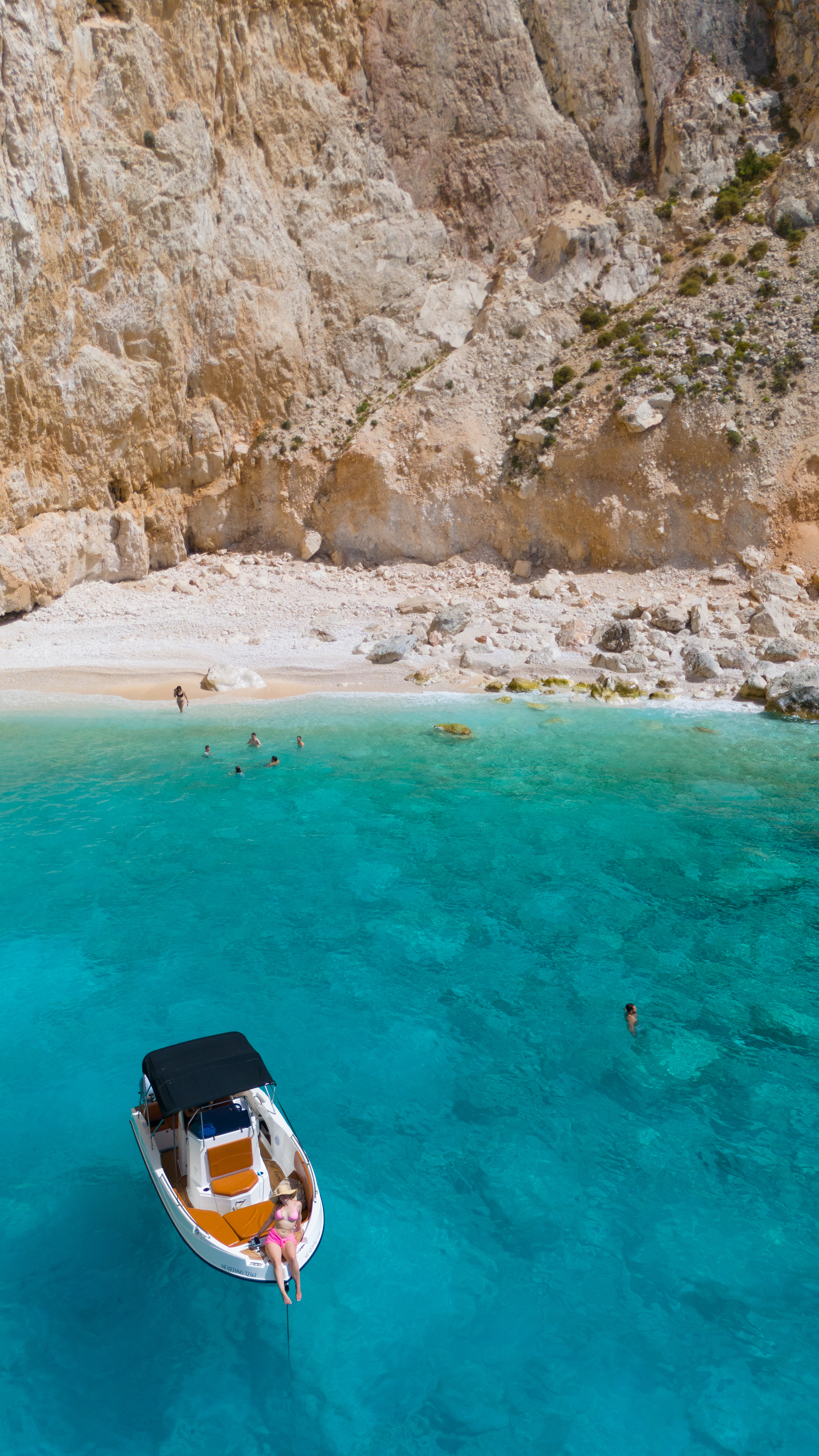 Aerial view of a small boat in a secluded turquoise cove along the Greek coastline