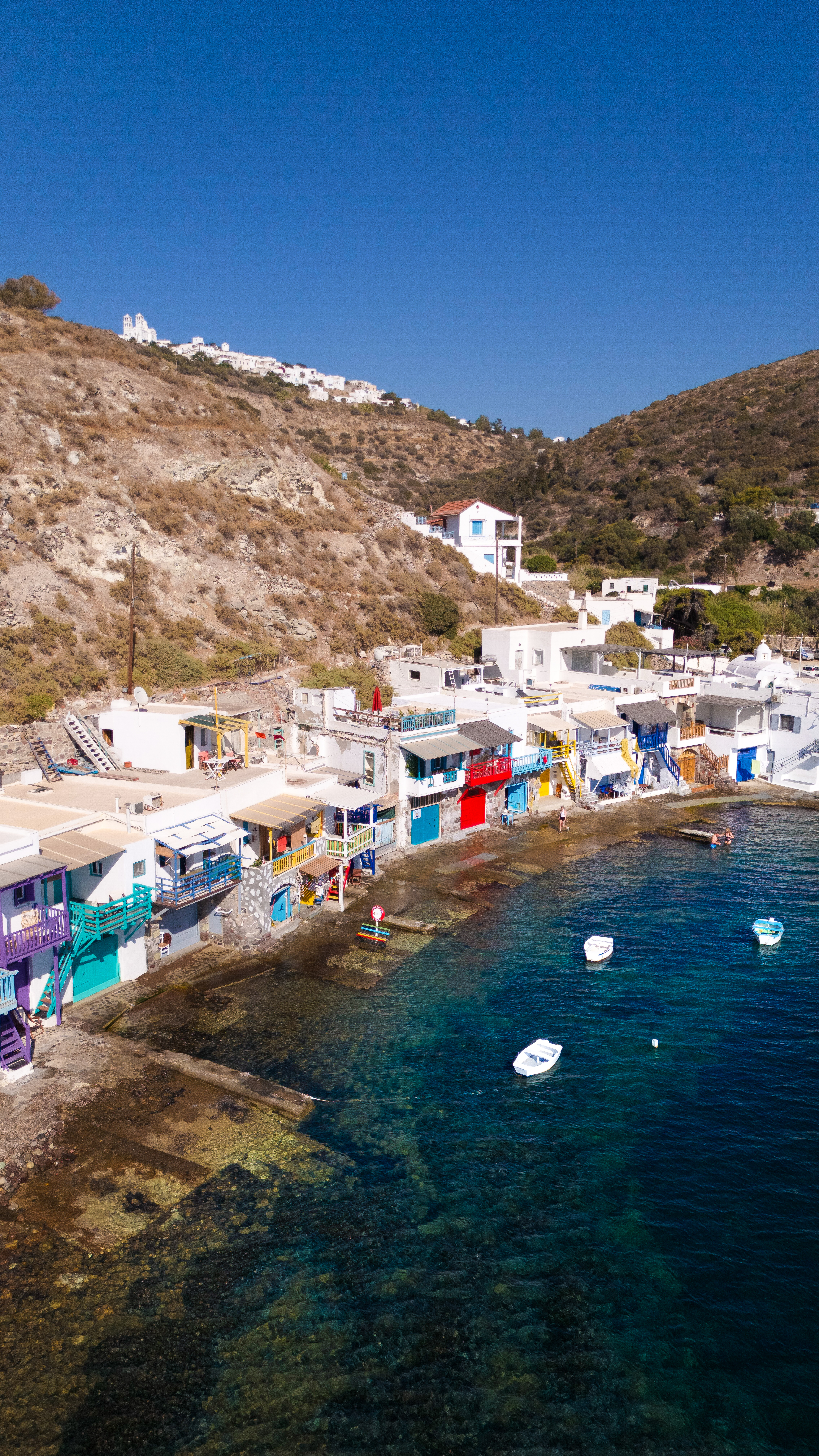 Aerial view of a white hilltop village overlooking the colorful harbor of Milos, Greece