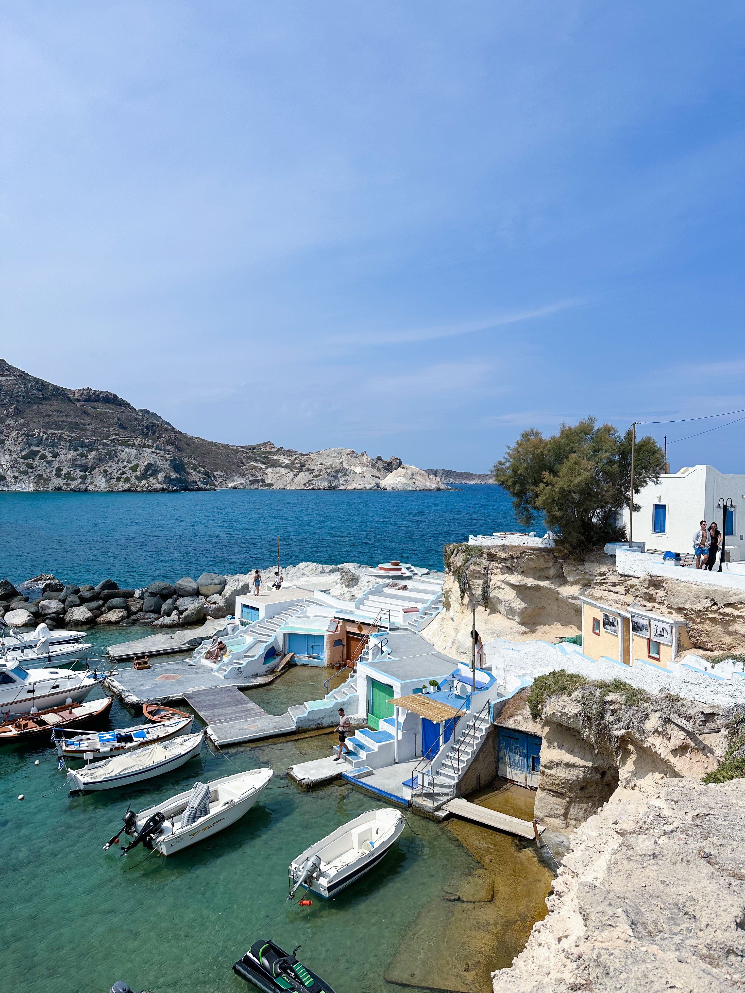 Colorful fishing boats docked in the turquoise harbor of Milos, Greece, beside whitewashed buildings