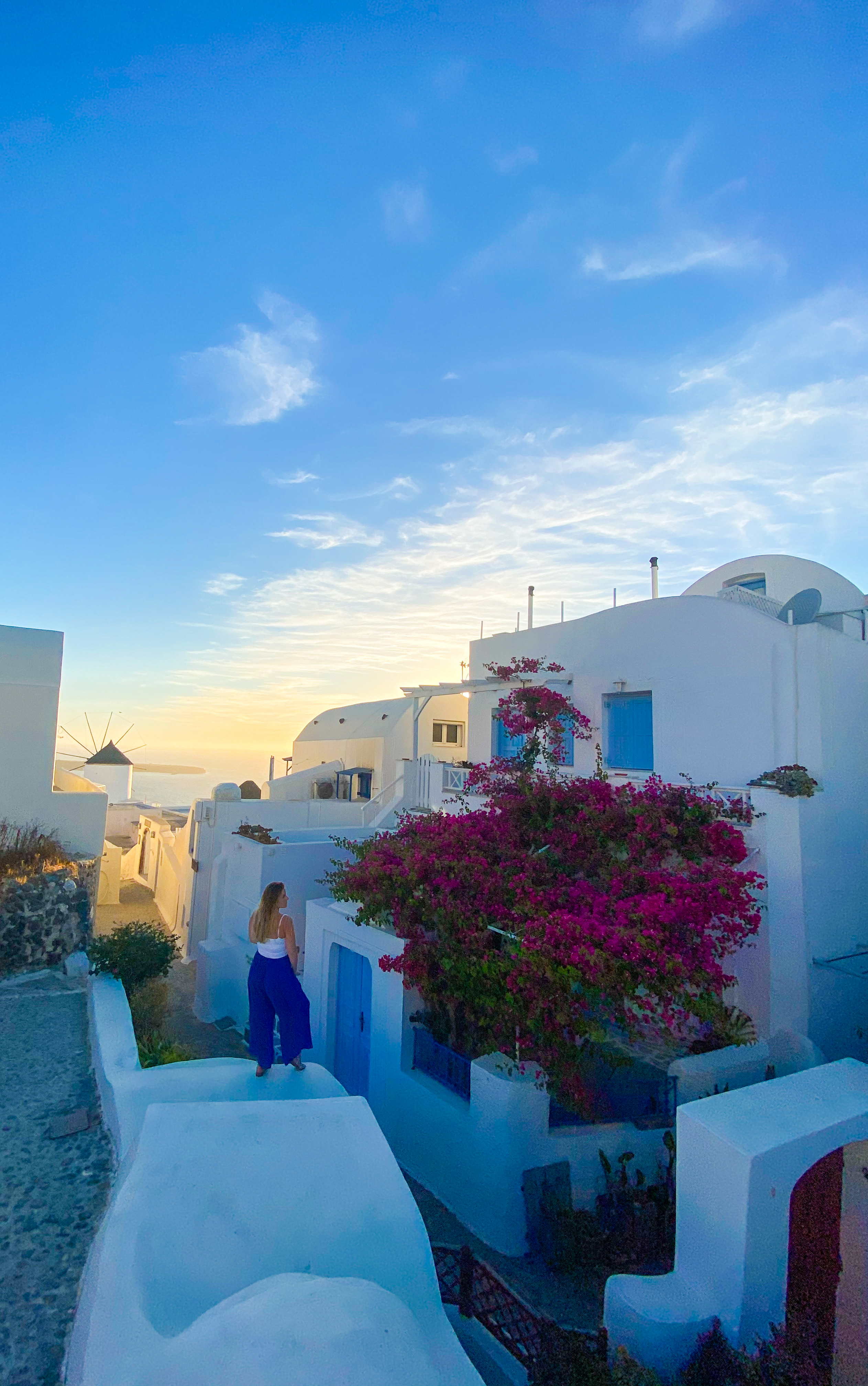 A traveler overlooking the whitewashed rooftops and windmill of Oia, Santorini at sunset
