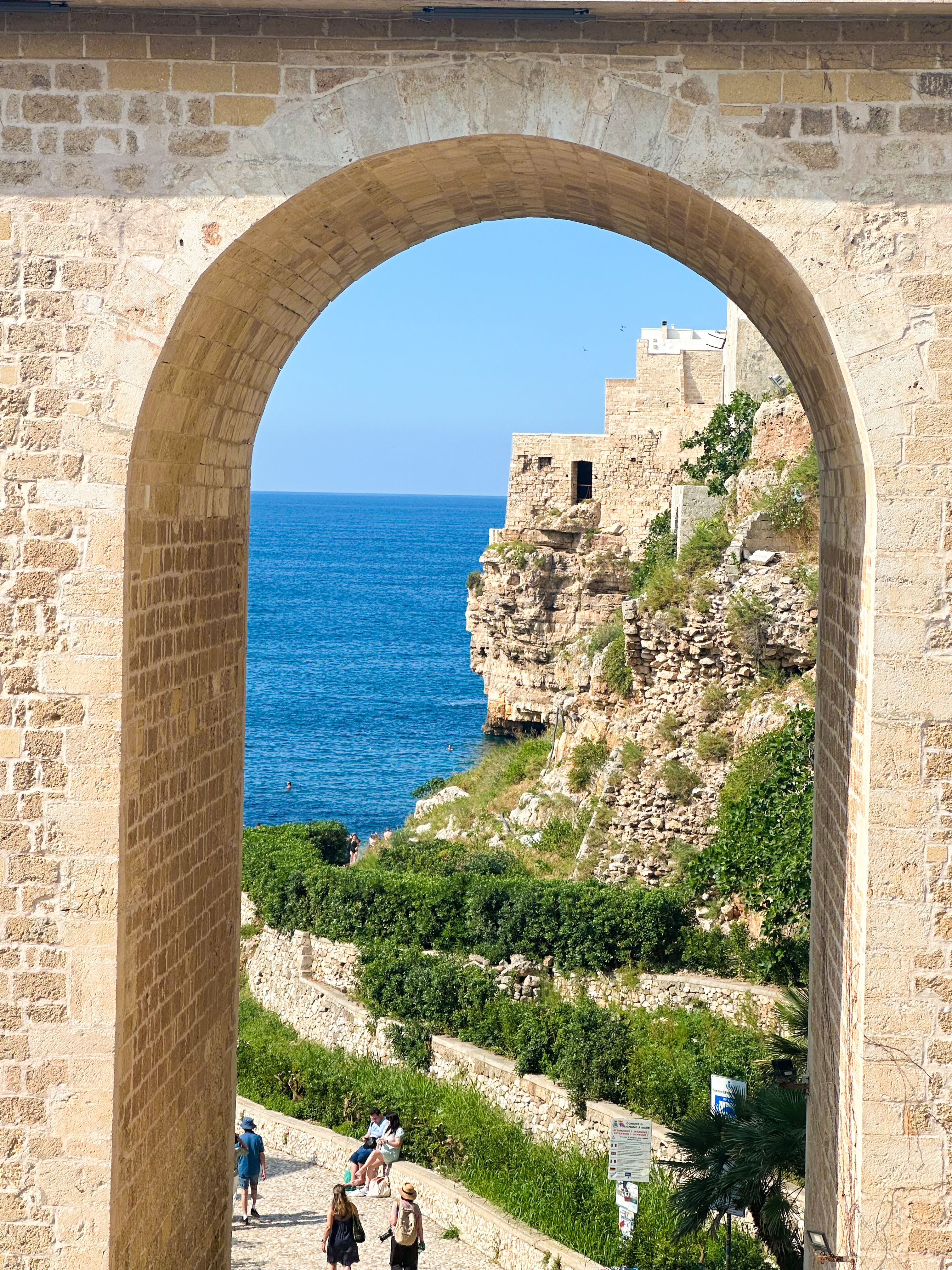 A stone archway framing a view of dramatic sea cliffs along the coast of Polignano a Mare, Italy