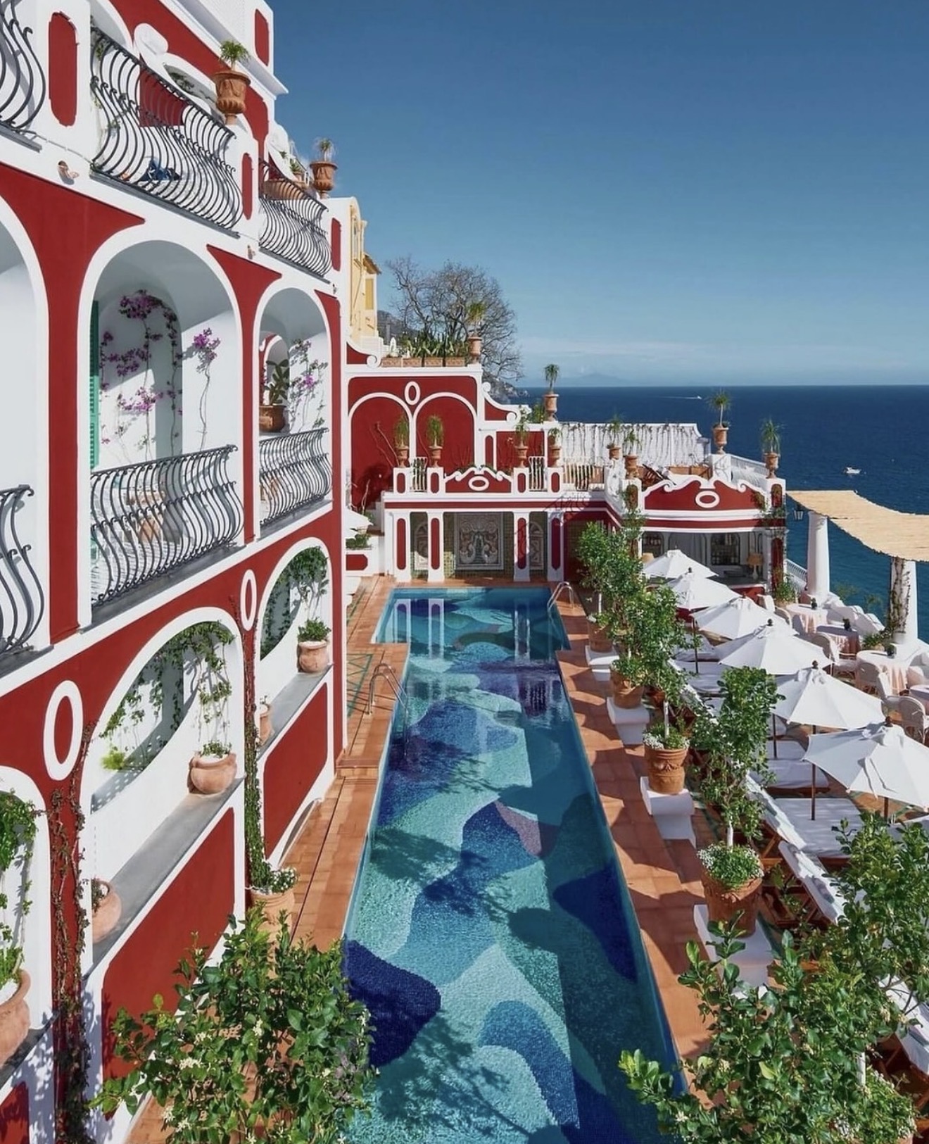 A mosaic-tiled infinity pool framed by the colorful cliffside facade of a Positano hotel