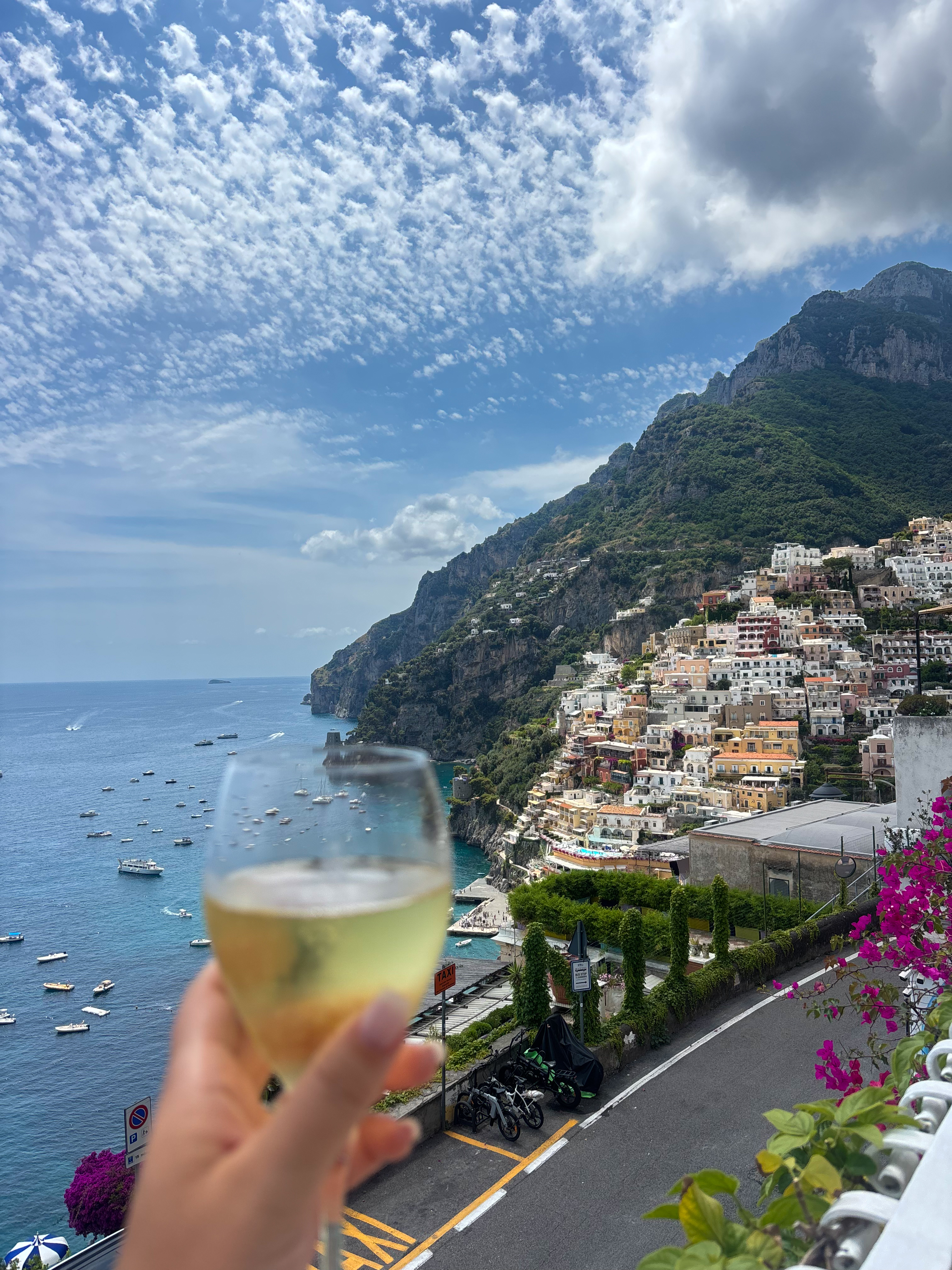 A glass of local wine raised against the cliffside view of Positano on the Amalfi Coast