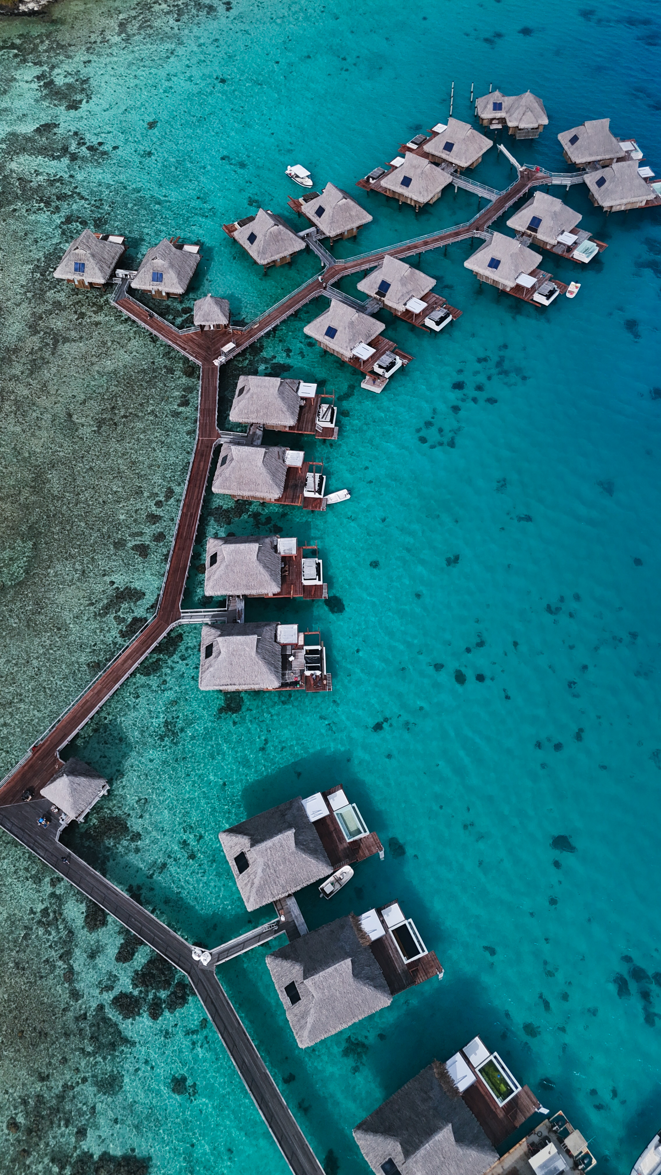 Aerial view of overwater villas connected by wooden walkways above a turquoise lagoon