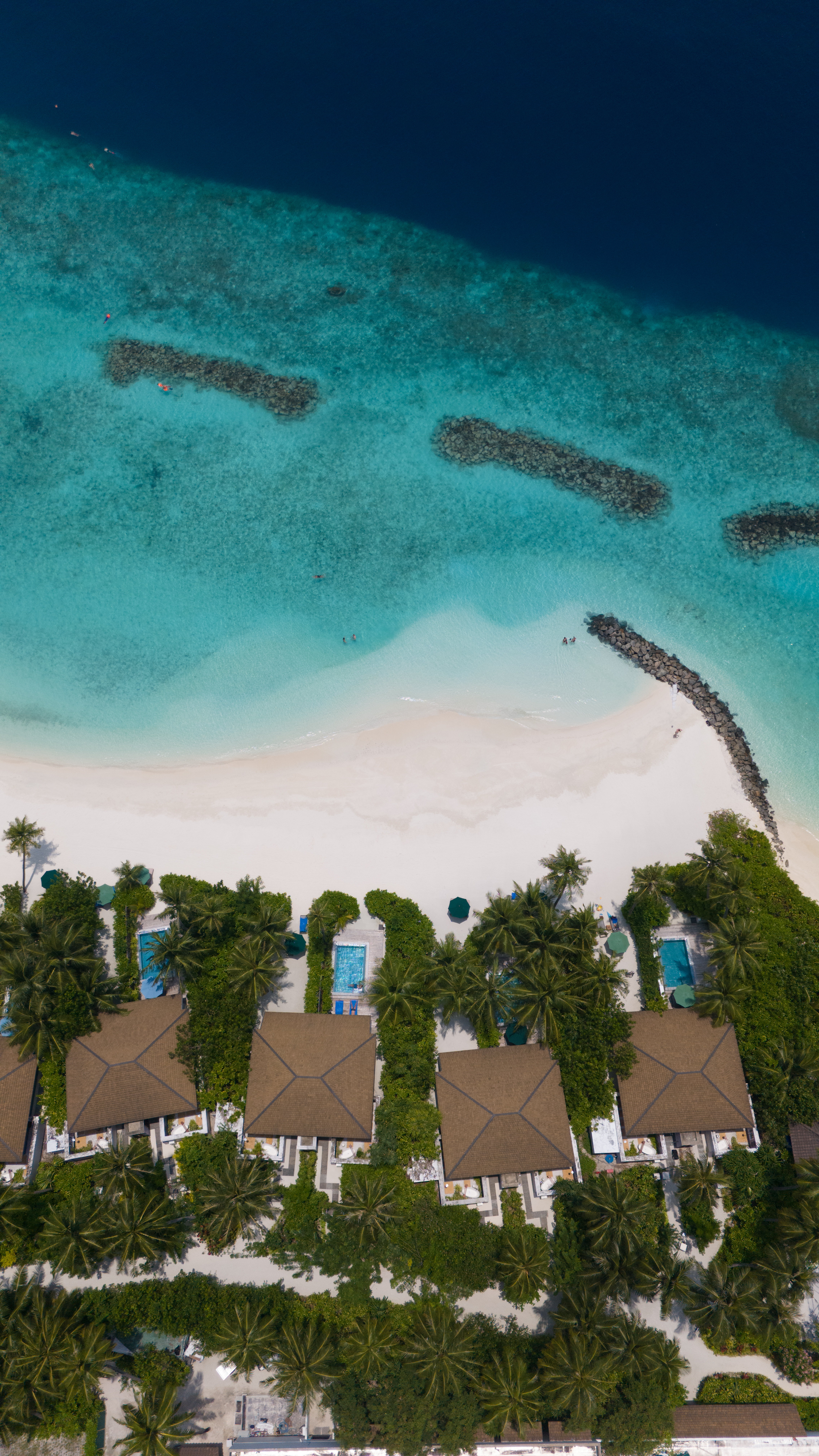 Aerial view of an overwater resort with thatched villas, palm trees, and turquoise water